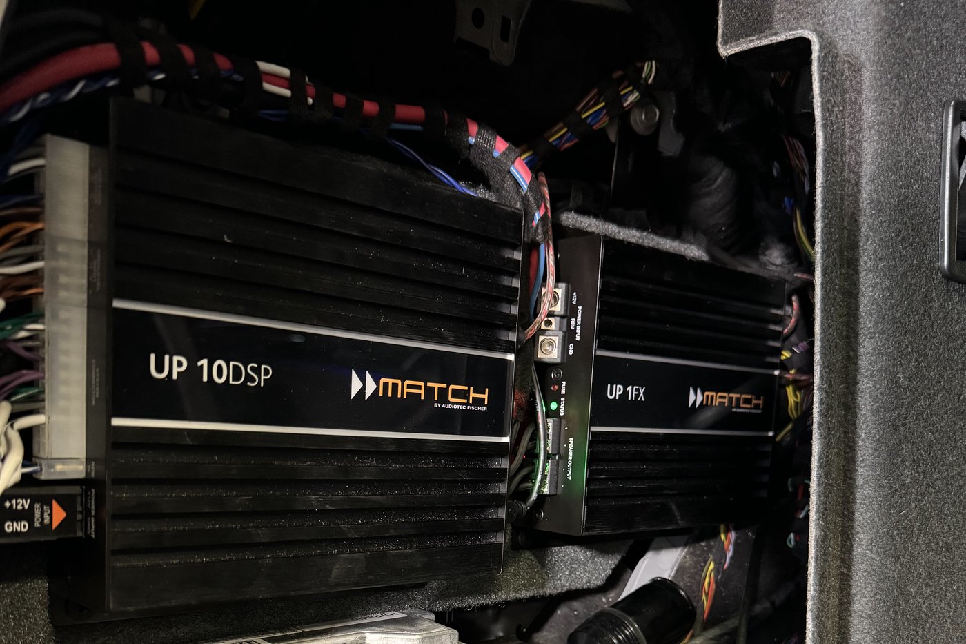 A Match UP 10DSP and a Match UP 1FX amplifier mounted side by side behind the trim of a BMW, wiring loomed back to the factory harness