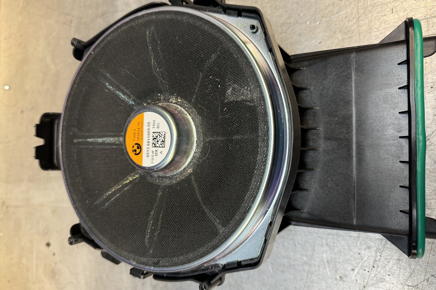 The factory BMW under-seat subwoofer, its paper cone still in the original moulded enclosure