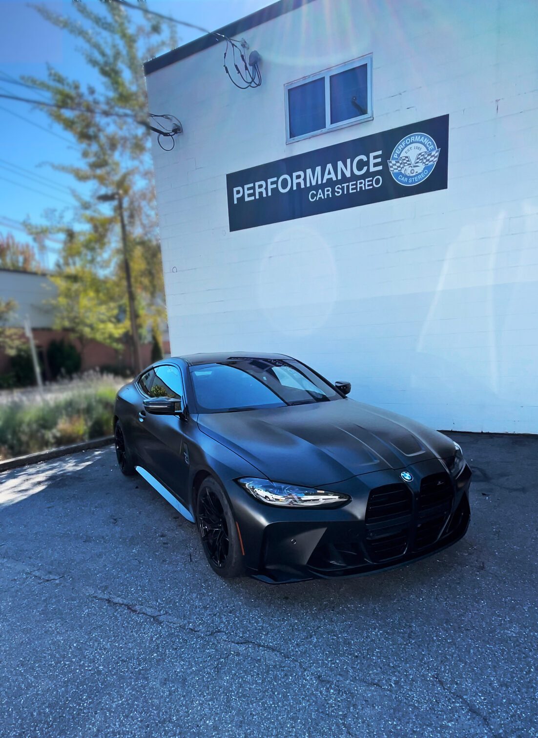 A matte black BMW M4 coupe parked outside the Performance Car Stereo building in North Vancouver