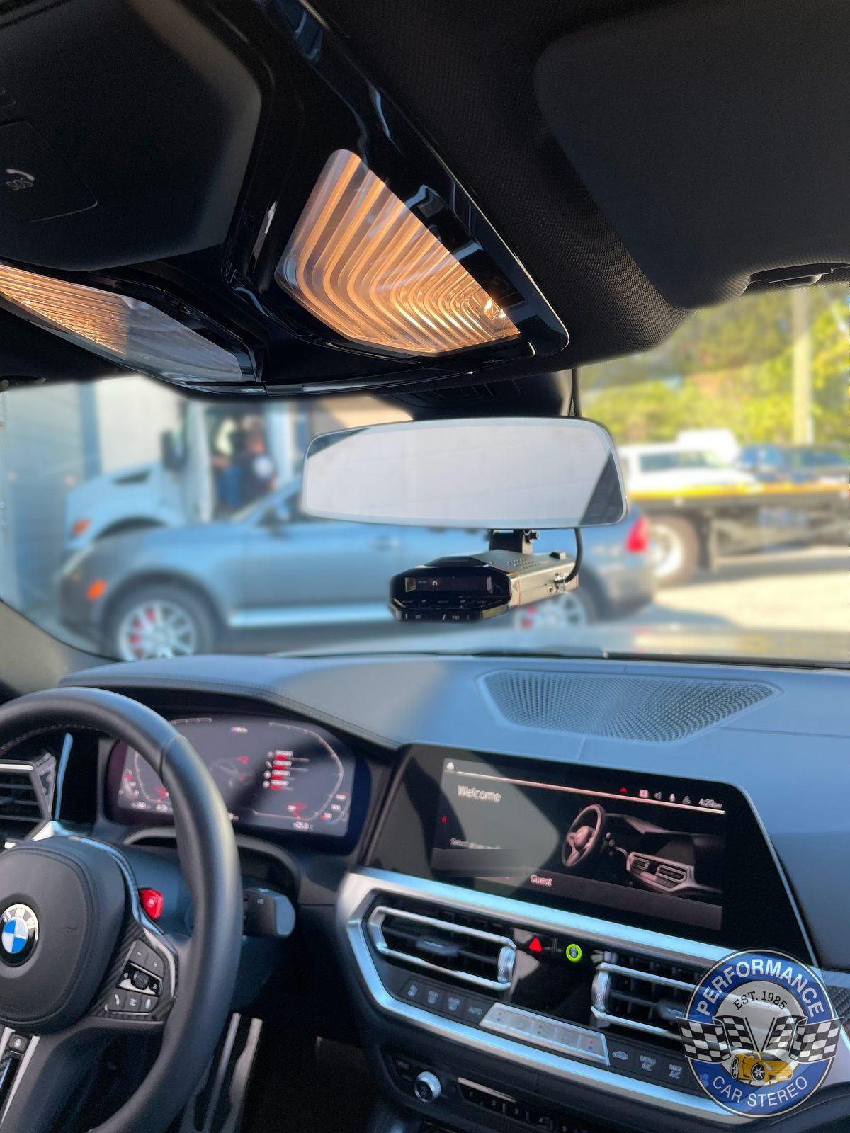View across the BMW M4's dashboard showing an Escort radar detector mounted below the rear-view mirror