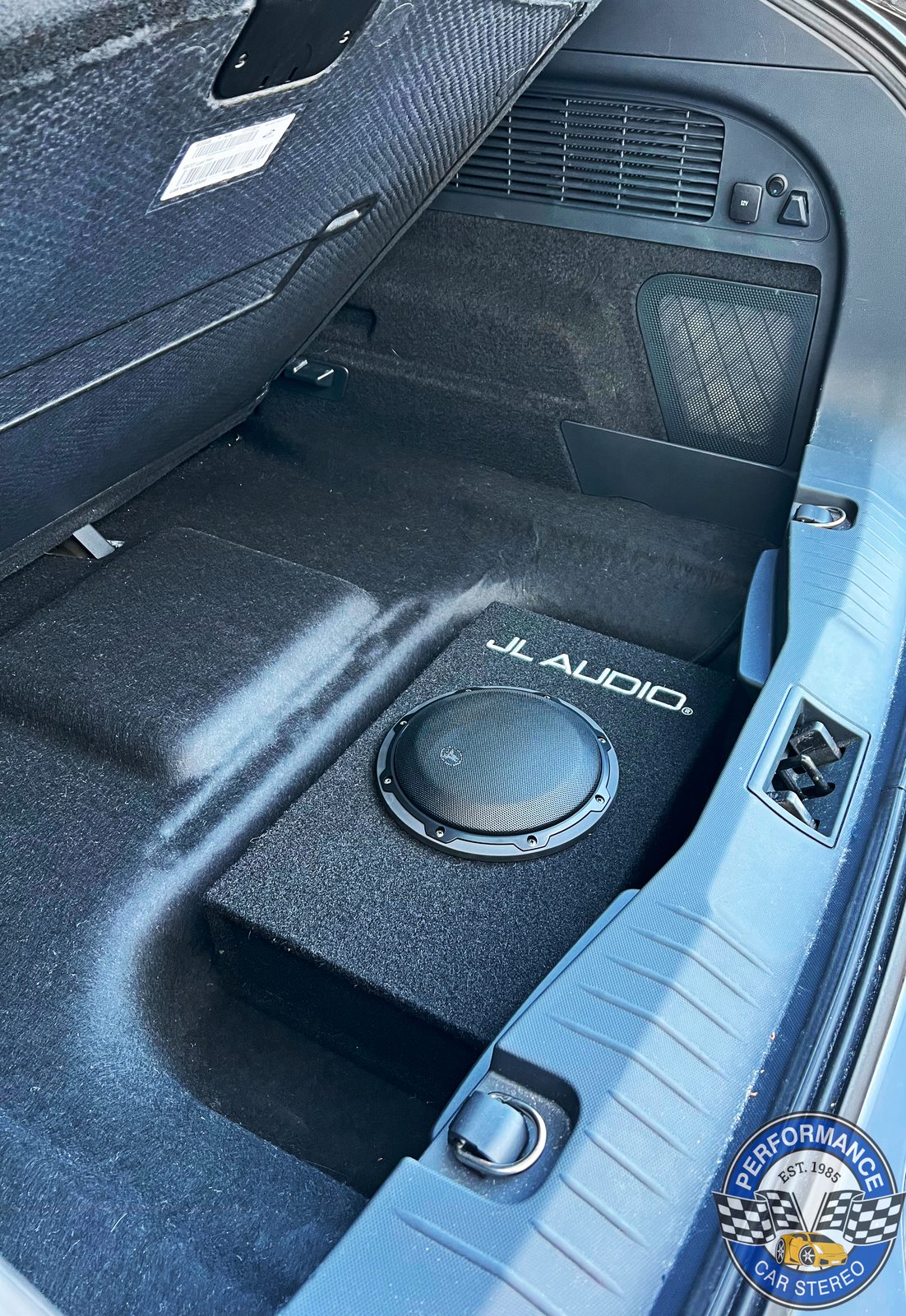 A JL Audio powered subwoofer enclosure sitting in the lower load area of the Mach-E, tucked against the side trim