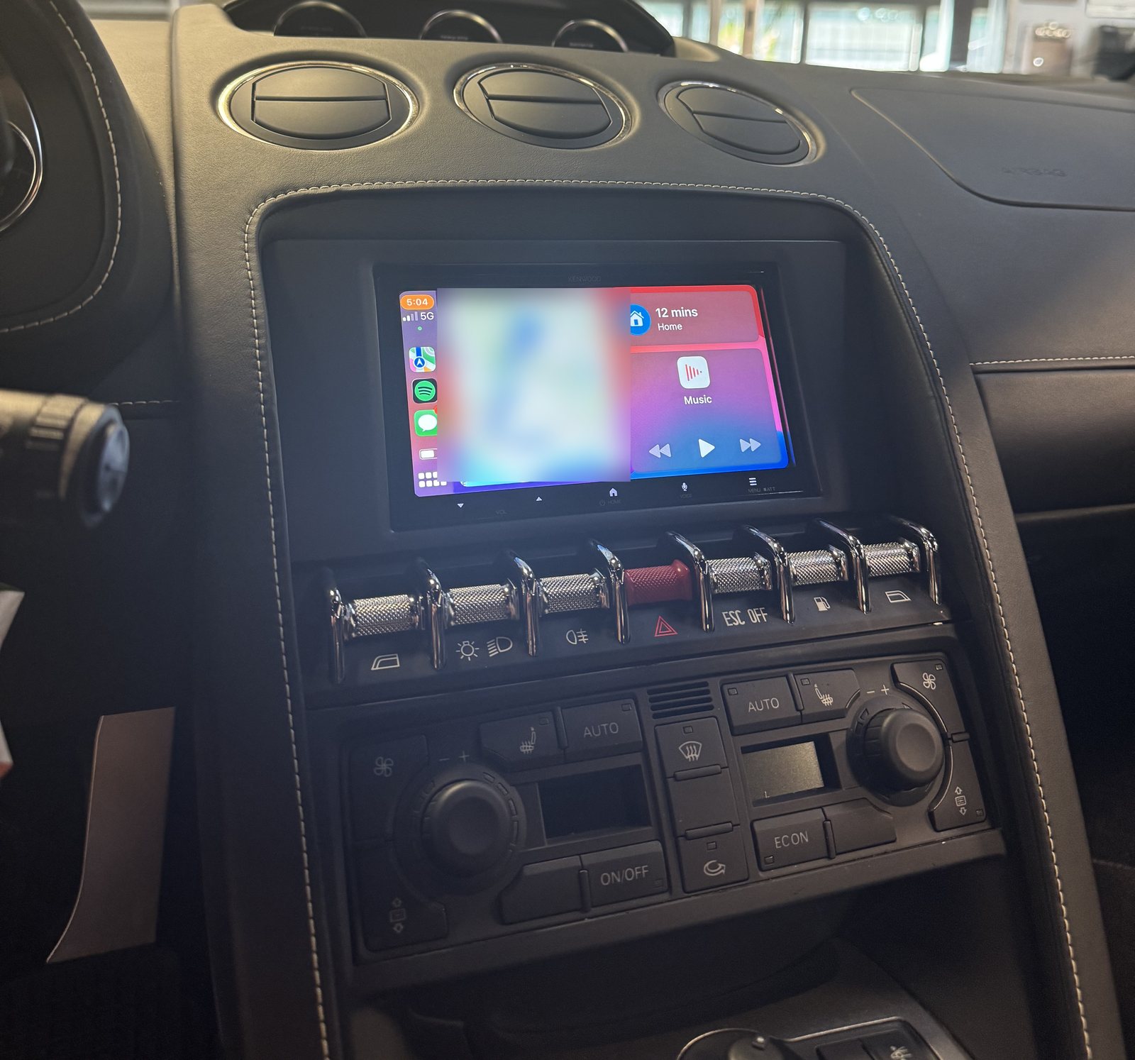 The Kenwood touchscreen running Apple CarPlay in the Gallardo's centre console, with the factory toggle switches and climate controls below it