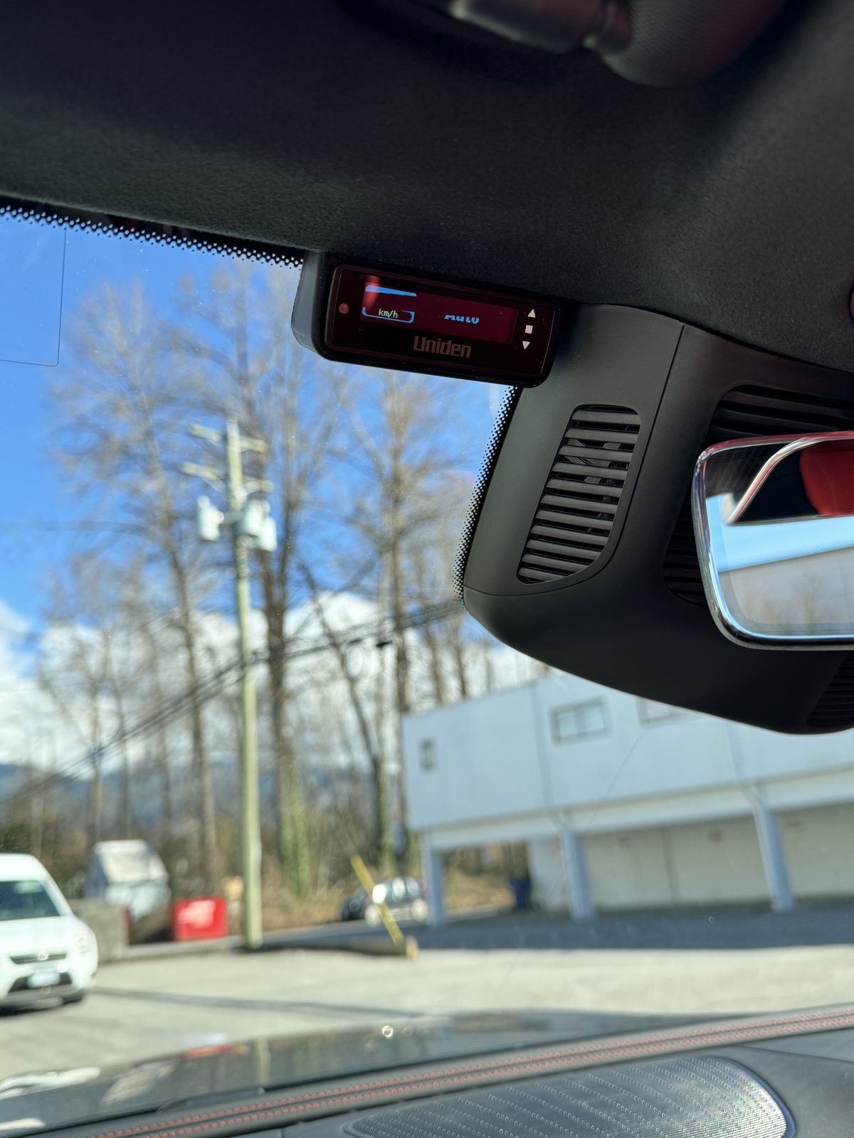 The Uniden R9W display mounted flush against the windscreen header beside the rear-view mirror, showing speed in km/h