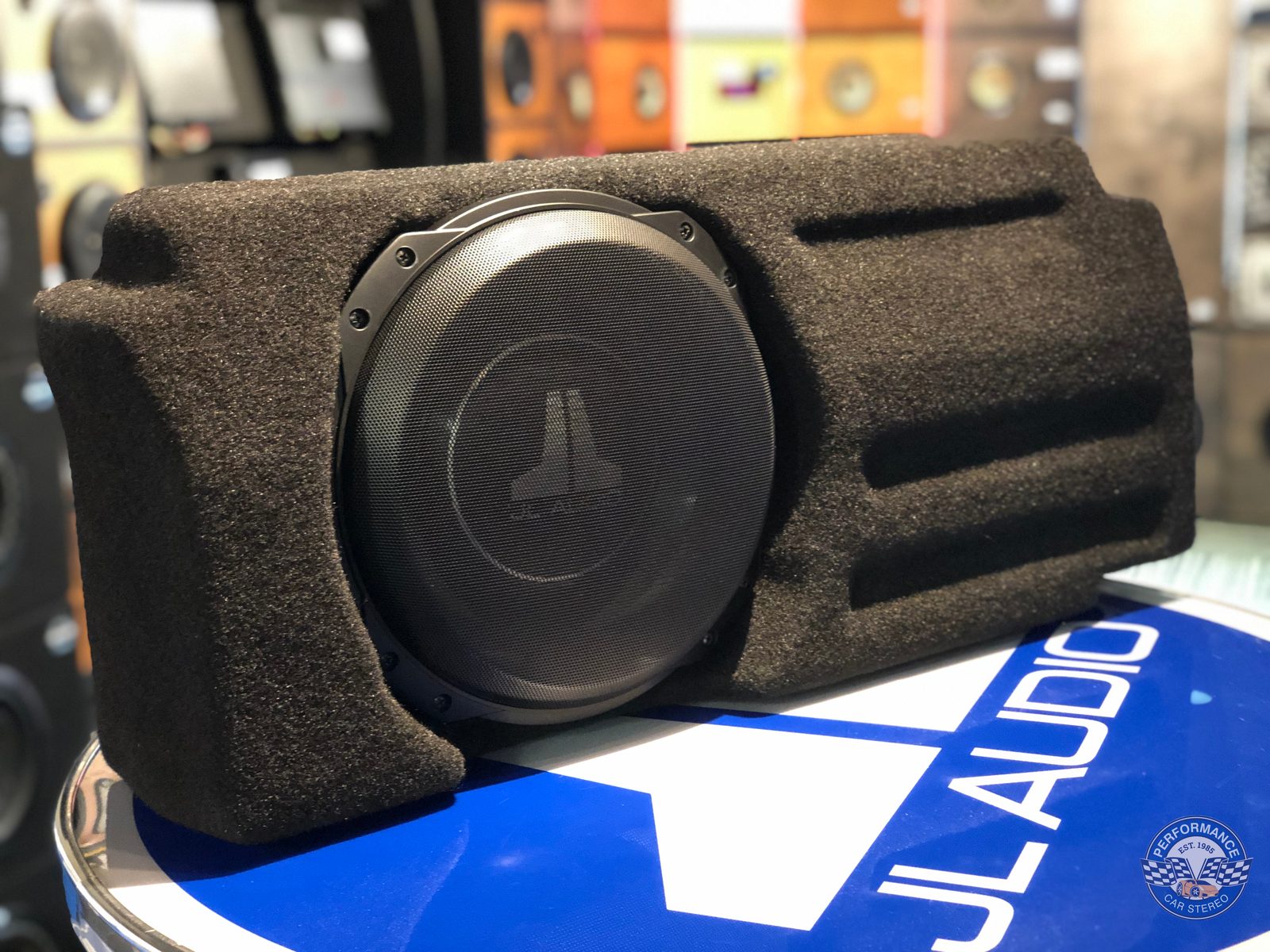 A JL Audio Stealthbox enclosure on the shop counter, its moulded fibreglass body shaped to match the contours of a Tacoma's rear cab wall