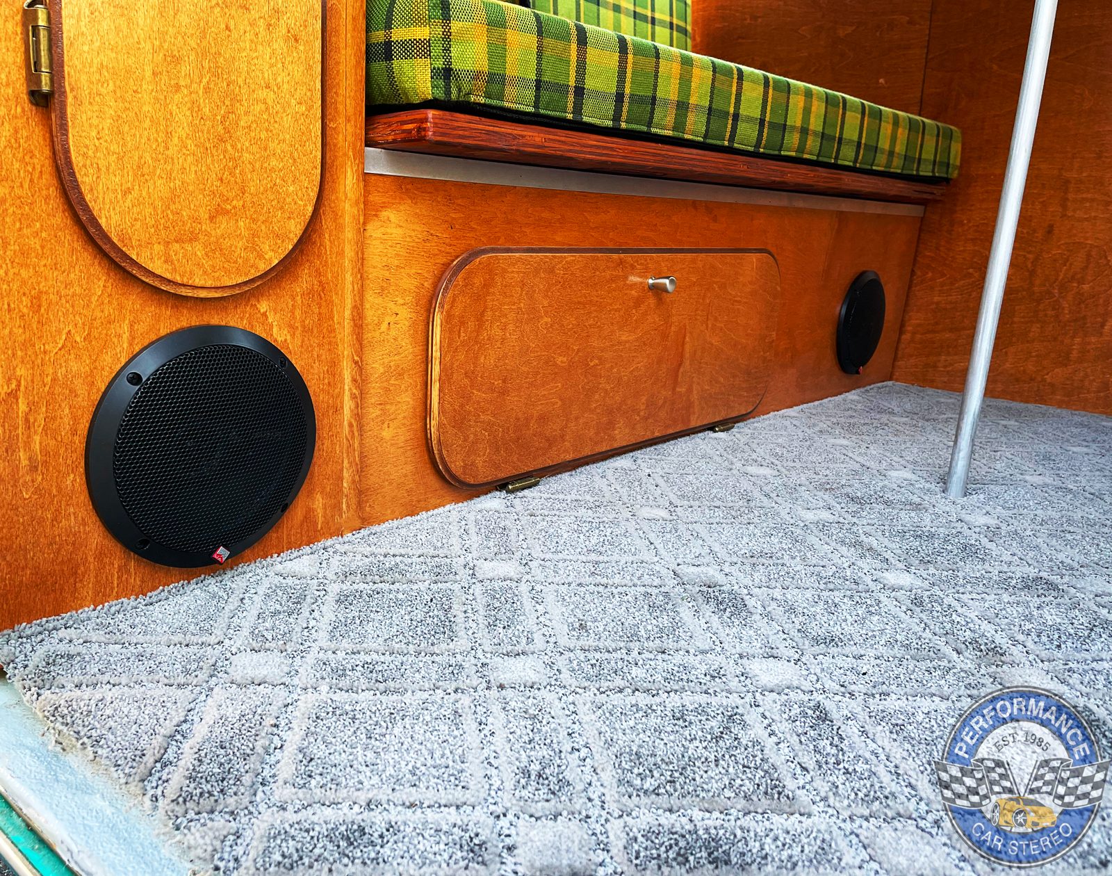 A Rockford Fosgate Prime coaxial speaker fitted flush into the varnished wood panelling below a plaid bench seat